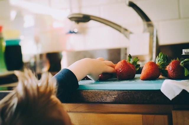 Child reaching for a strawberry in the kitchen